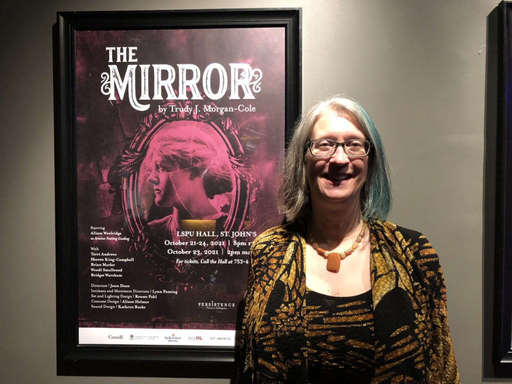 Une femme est debout à côté d'une affiche publicitaire pour la pièce de théâtre The Mirror. 

