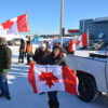 Un groupe de personnes, trois avec des drapeaux du Canada rouge et blanc à la main.