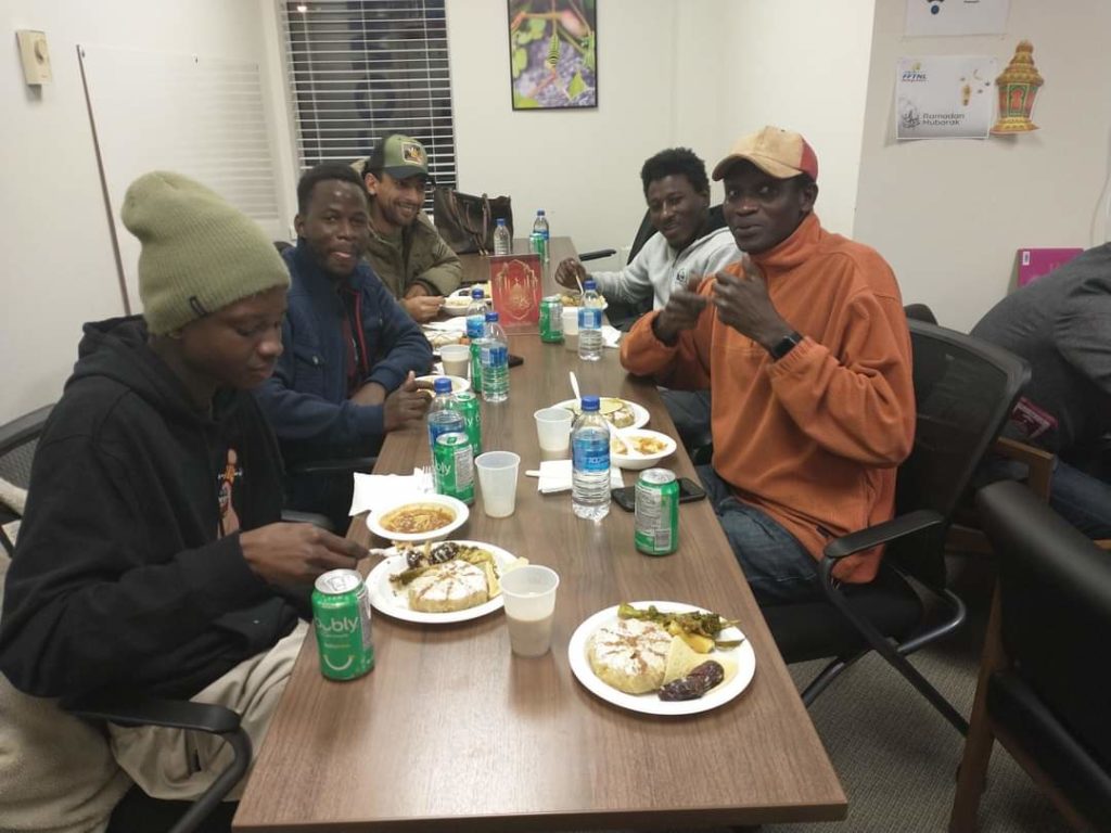 Plusieurs hommes sont autour d’une table de bois en train de manger un diner. 