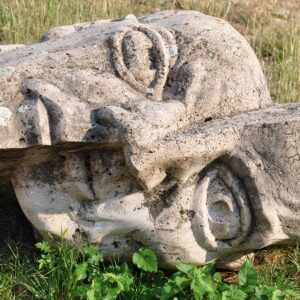 Une sculpture en pierre d’un visage couper en deux qui repose sur de l’herbe. 