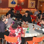 Un groupe de personnes sont assises et mangent à des tables rondes dans une sale avec des décorations de Noël.