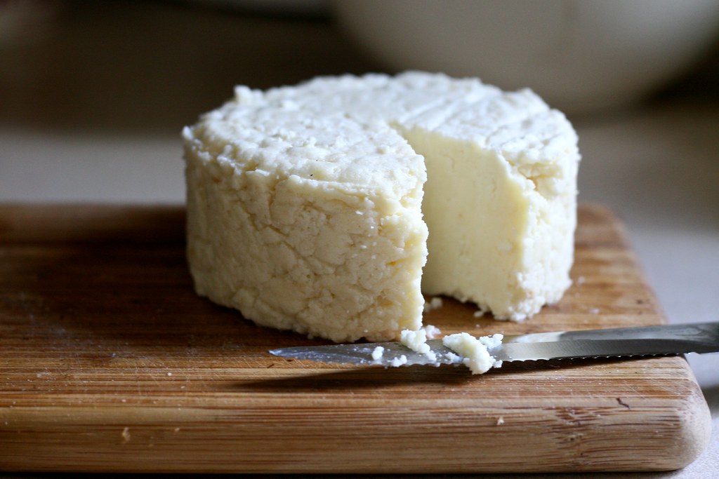 Un morceau de fromage fait maison et un couteau sur une planche en bois.